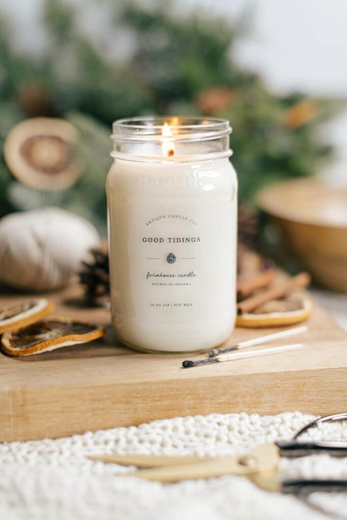Lit candle on a wooden board surrounded by greenery and sliced dried oranges