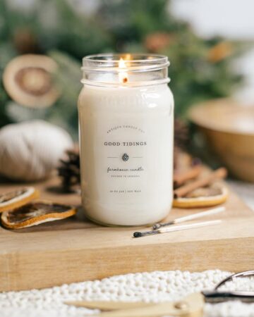 lit candle on wooden board surrounded by greenery and cozy items
